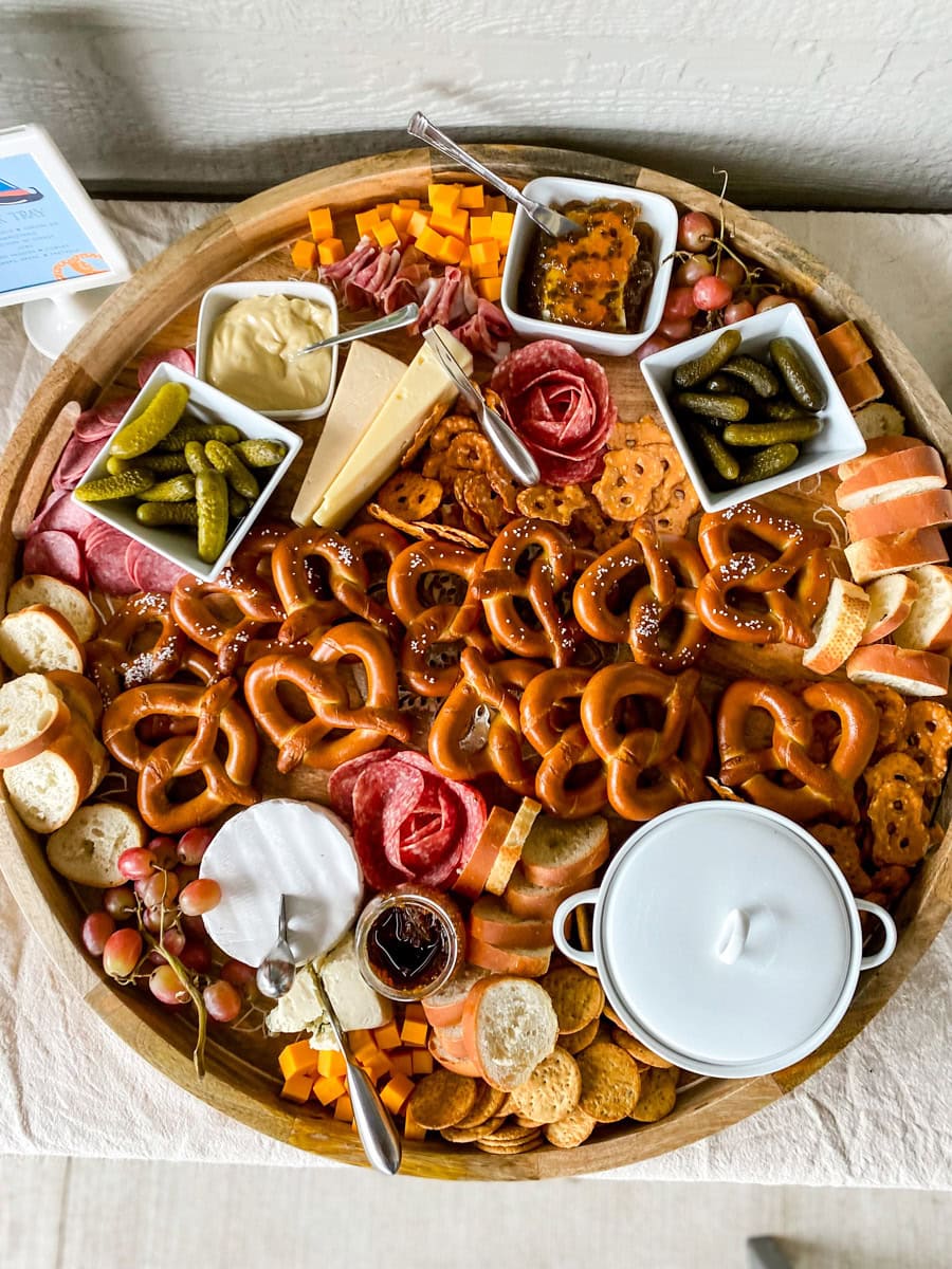 Overhead view of adult Oktoberfest party charcuterie and pretzel board with salami, cheese, pickles, jam, and soft pretzels