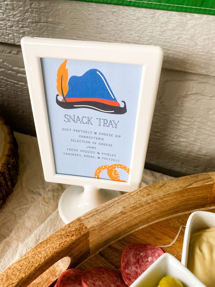 Snack Tray printable sign next to adult Oktoberfest party charcuterie board with salami and pickles