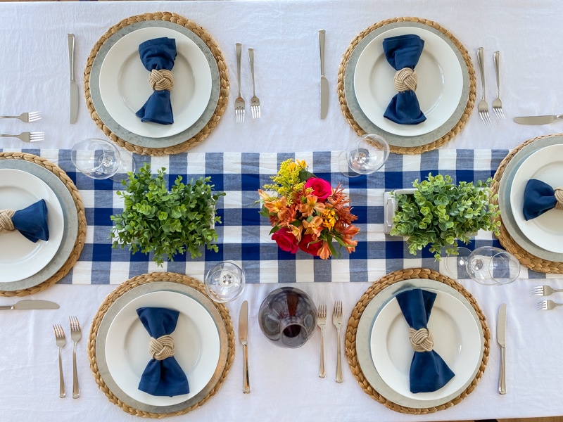 Overhead view of Thanksgiving table with bright florals, greenery, and blue buffalo check table runner