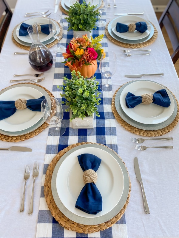 Thanksgiving table with bright florals, greenery, blue buffalo check table runner, and blue linen napkins