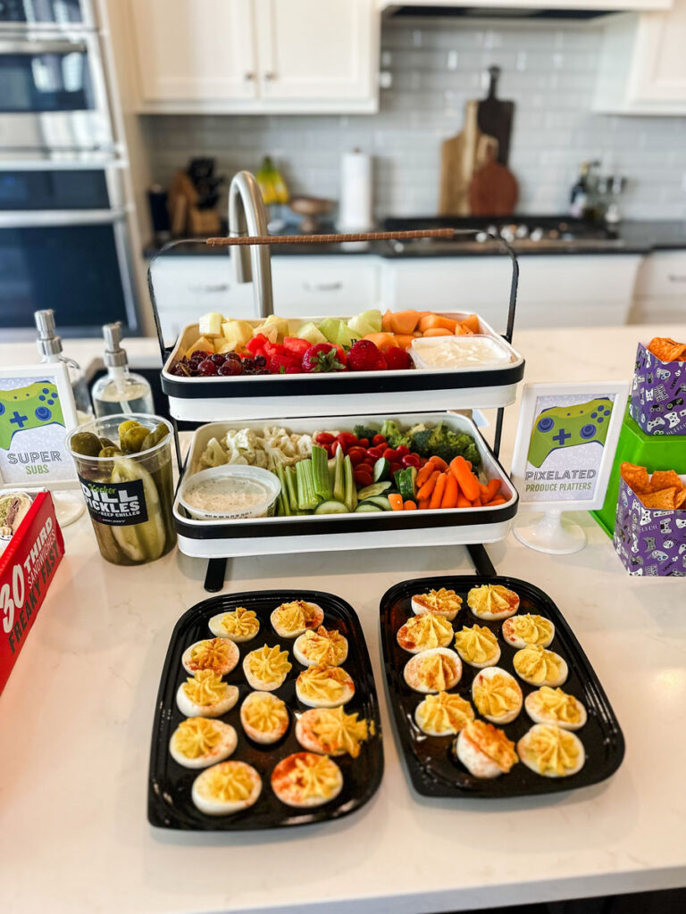 Pixelated Produce Platters" framed sign next to two-tiered fruit and veggie platter and individual gaming-print chip boxes at gamer birthday party