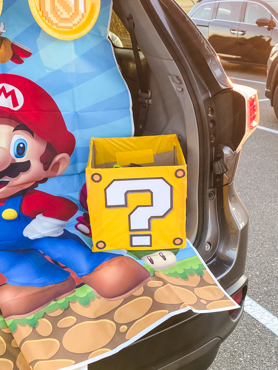 DIY yellow Mario question mark block candy box made from construction paper and a printed question mark, sitting in a trunk or treat display
