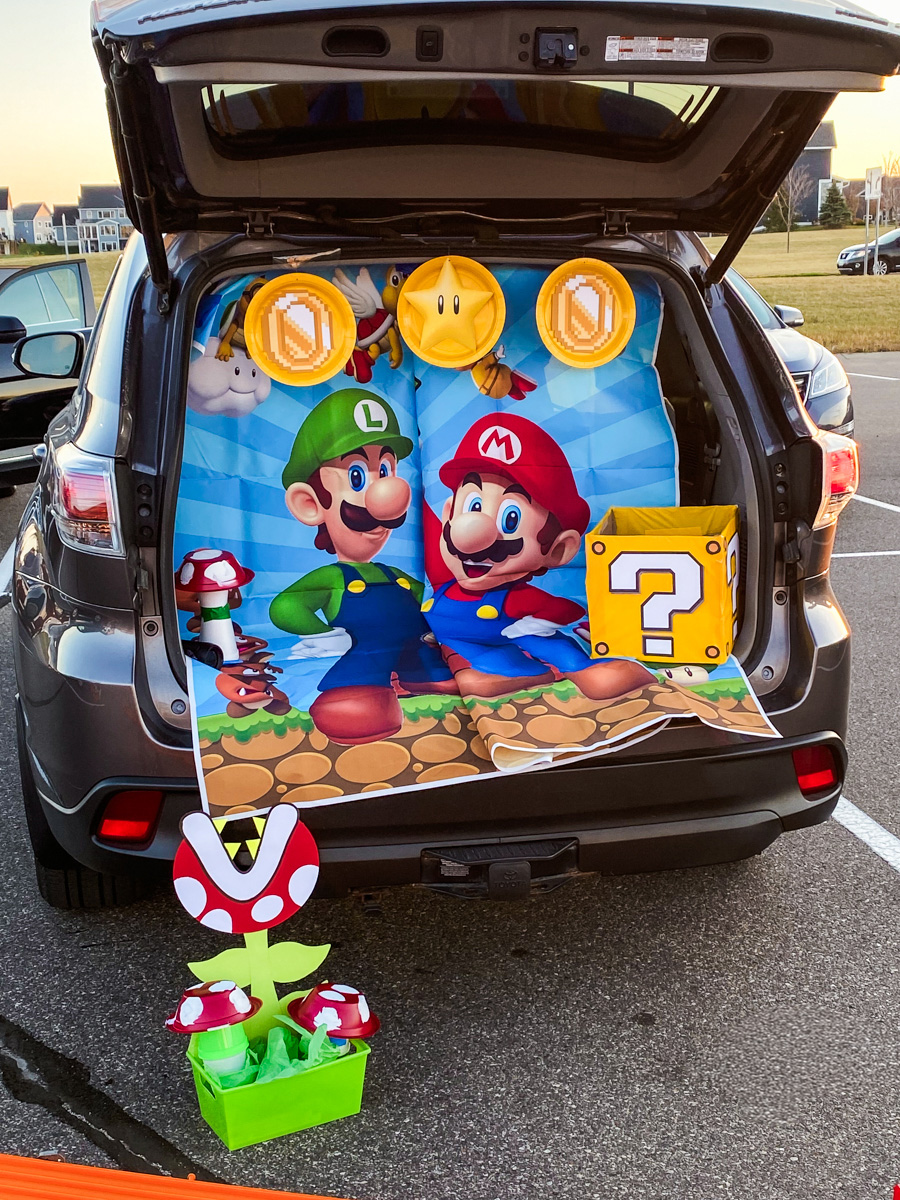 Super Mario trunk or treat backdrop with Mario and Luigi, gold coin paper plates, a yellow star, and a question mark box in the back of an SUV