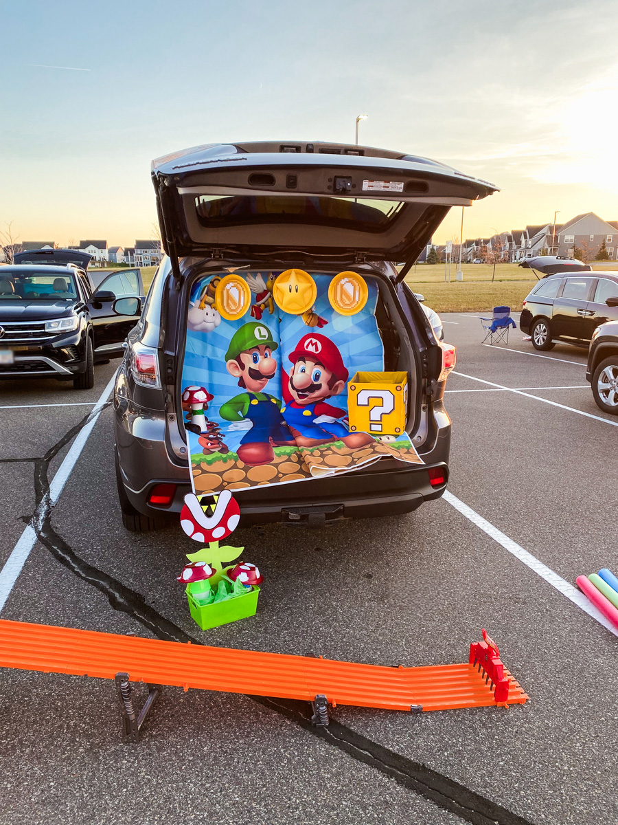 Full Mario trunk or treat setup with Hot Wheels six-lane race track in front of an SUV decorated with a Super Mario backdrop and DIY piranha plant