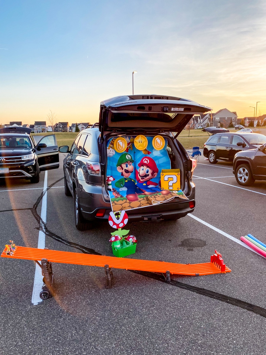 Wide sunset view of a Mario Kart trunk or treat with a Hot Wheels race track in a school parking lot