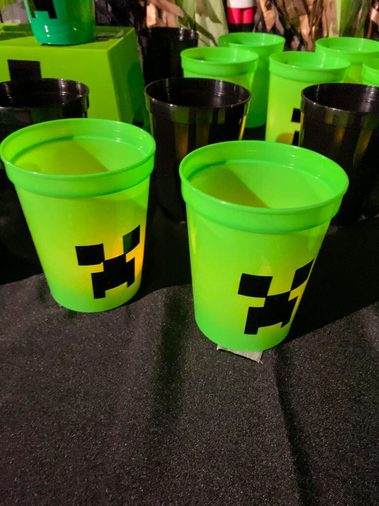 Close-up of green Creeper Cup game cups with battery tea lights glowing inside for a Minecraft trunk or treat