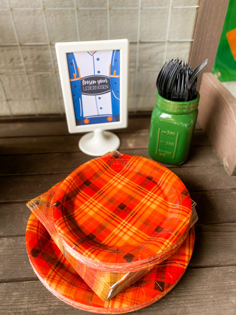 Loosen Your Lederhosen printable sign next to plaid paper plates and napkins at an adult Oktoberfest party