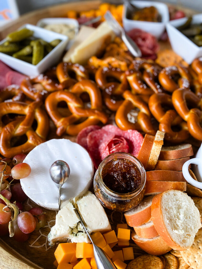 Close-up of adult Oktoberfest party charcuterie board with brie, cheddar, fig jam, and salami rosettes