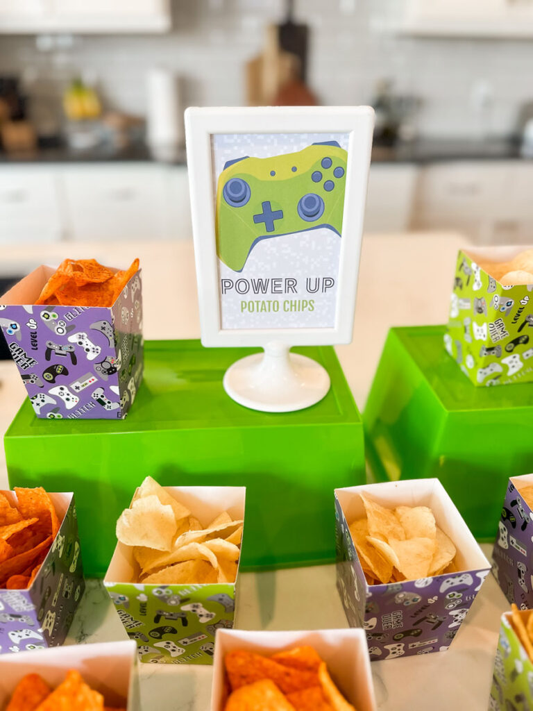 "Power Up Potato Chips" sign surrounded by individual lime green and purple gaming-print chip boxes at gamer birthday party Power Up Station