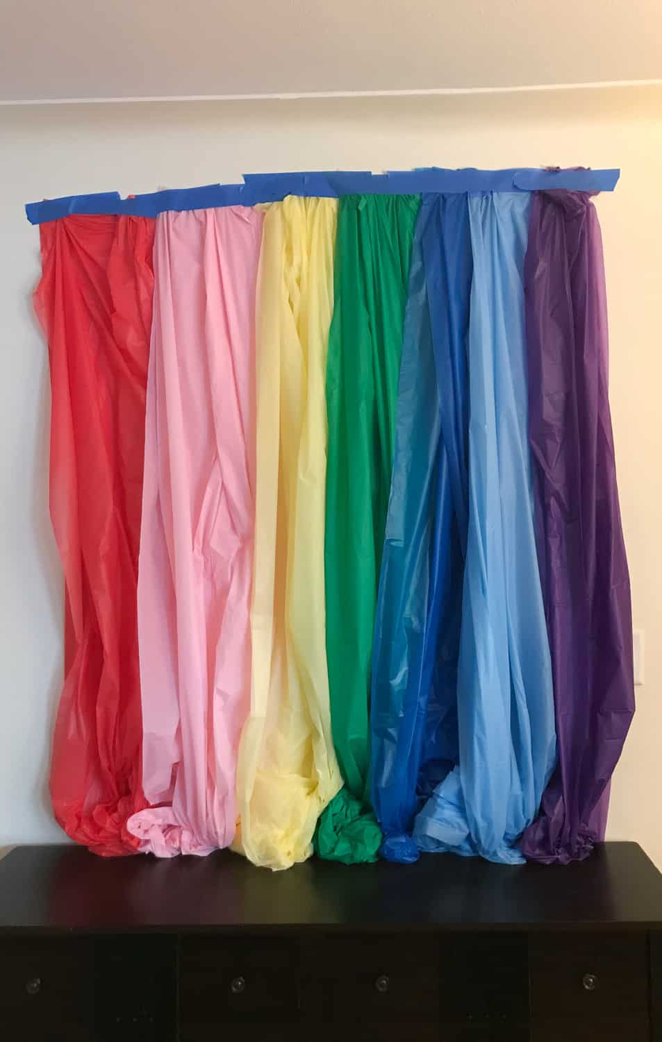 Tape the plastic table clothes to the wall to create a DIY rainbow backdrop for St. Patrick's Day