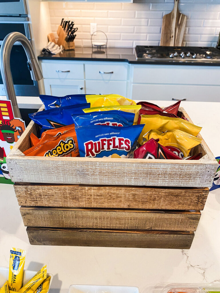 Wooden crate filled with individual snack bags including Ruffles and Cheetos at Roblox birthday party food station