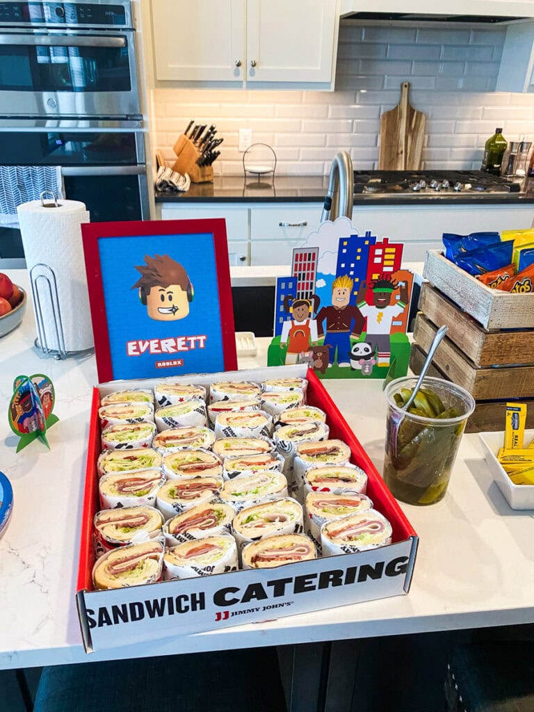 Jimmy John's sandwich catering box with Roblox character standees at Roblox birthday party kitchen island