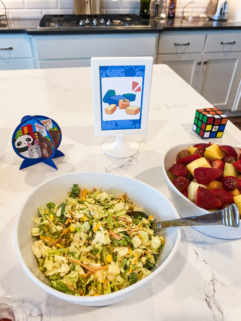 Asian salad and fresh fruit bowl with Roblox game food label sign at Roblox birthday party kitchen island