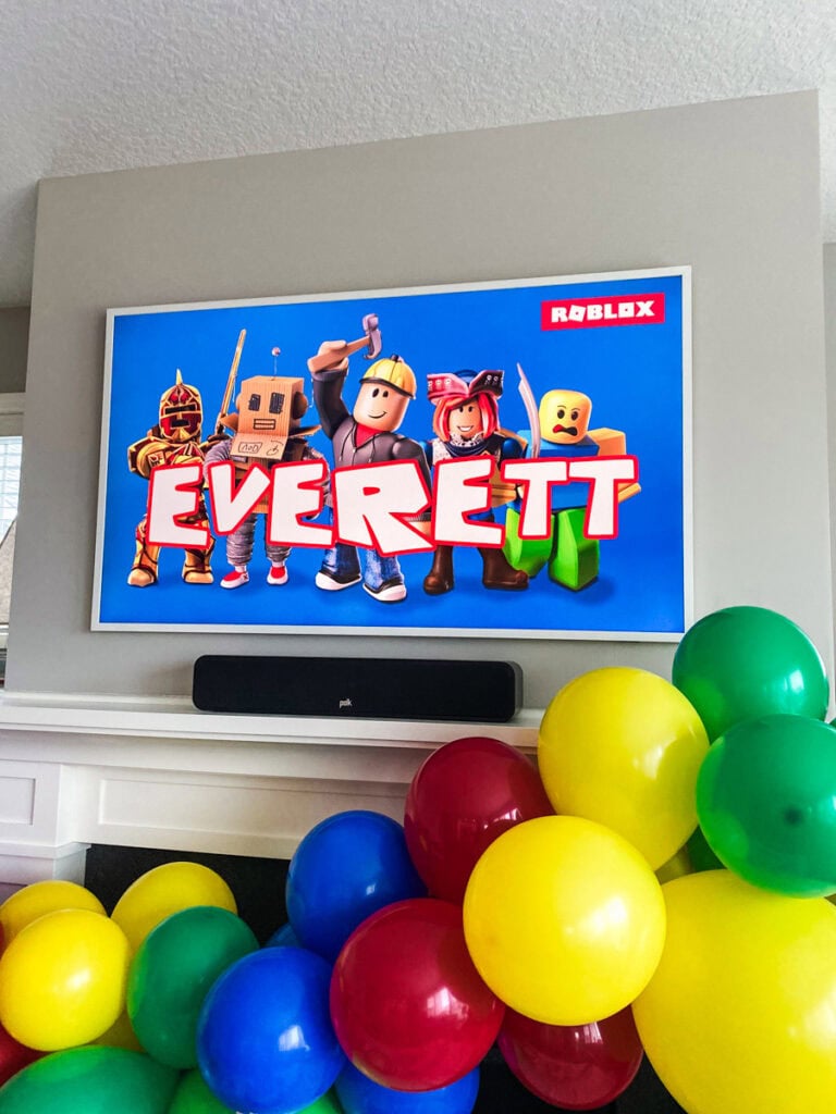 Frame TV displaying custom Roblox birthday party graphic with Everett's name in Roblox font and colorful Roblox characters on blue background