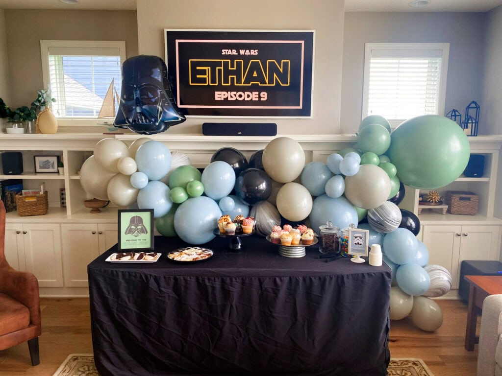 Muted Star Wars birthday party dessert table with dusty blue and sage green balloon garland, cupcakes, and Star Wars printable signs
