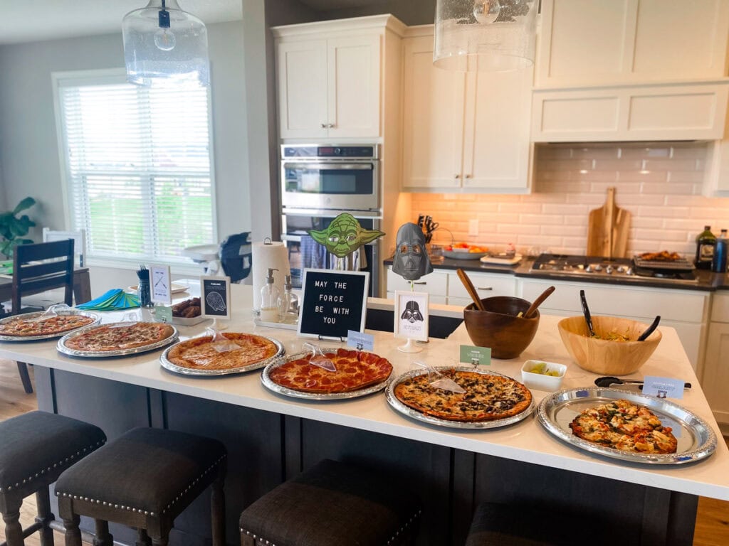 Star Wars themed pizza buffet on kitchen island with Yoda sign, May the Force Be With You letter board, and food tent cards